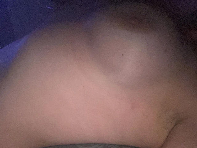 Melli-hot's bare chest, showing small, perky tits with light brown areolas and nipples, in a dimly lit, close-up shot. Visible lower belly and subtle pubic hair.