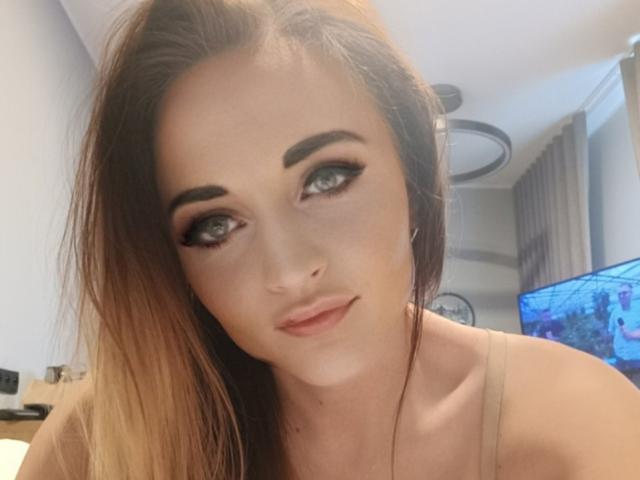 NicoletteCreazy has light brown hair, blue eyes, and is looking up with a slight smile. She's wearing a beige top and has a cute, sexy face.