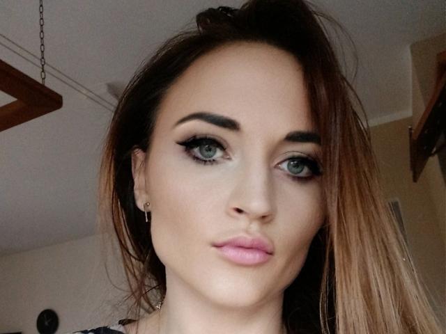 NicoletteCreazy has green eyes, dark eyebrows, pink lips, and brown hair, wearing black eyeliner, looking straight at the camera with a slight pout.