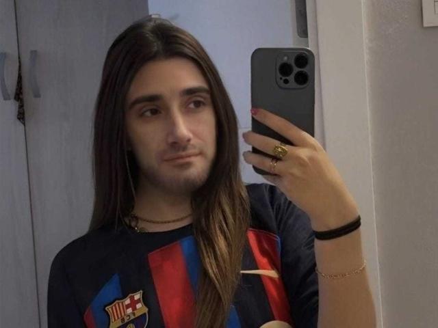 JodyTs with long brown hair, wearing a Barça shirt, taking a mirror selfie with a grey iPhone, gold ring, and bracelet, looking slightly bored.