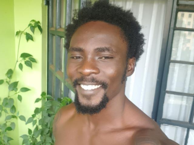 TheBlackStallionn has dark brown skin, a short curly Afro, a thin black goatee, and is shirtless, smiling with white teeth, and has a lean, muscular build.