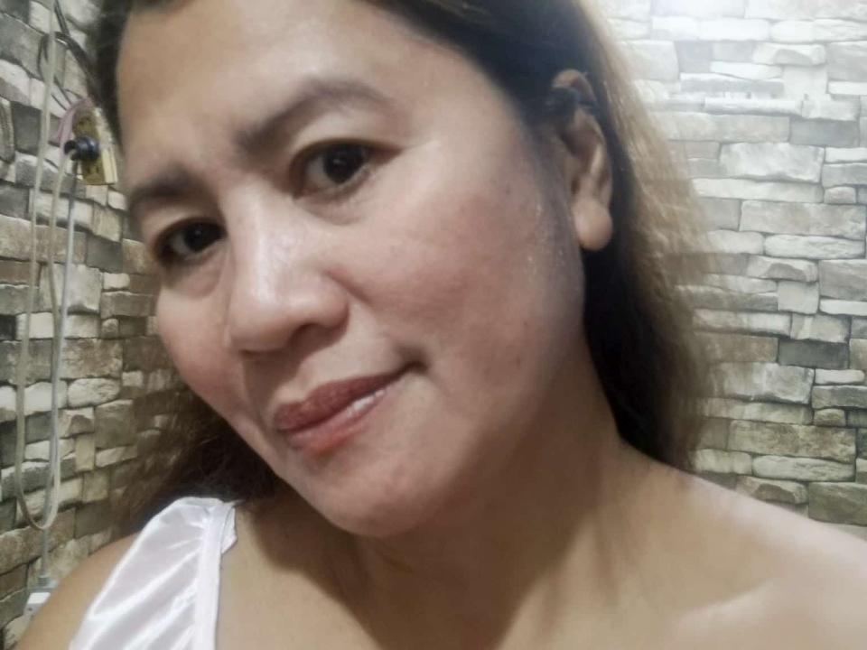 Hannahh69 has a cute smile with slightly flushed cheeks, brown eyes, and light brown hair. She's wearing a white strap, showing her bare shoulders and soft skin.