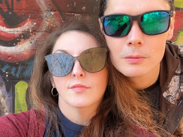 Cermisyy with brown hair, wearing black sunglasses and a red sweater, stands next to Cermisyy with green sunglasses and a brown shirt. Both have serious expressions.