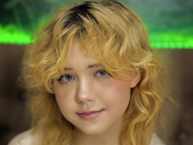 EmilyAngels has curly blonde hair, blue eyes, and a cute face with a slight smile. She's looking directly at the camera with a gentle, innocent expression.