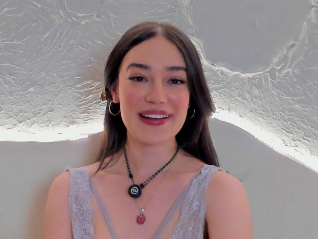 MariaLoft has long brown hair, wearing a lace gray top, hoop earrings, black necklace with red pendant, smiling with pink lipstick, showing her tits, and a cute face.