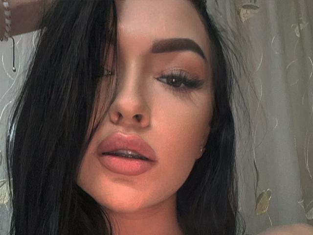 SashaLorenz has dark, wet hair covering one eye, full pink lips, and thick, arched eyebrows. She's wearing subtle makeup and has long, black lashes.