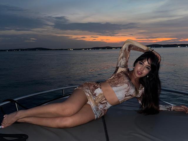 Heyly lies on a boat at sunset, wearing a sheer, bejeweled crop top and matching shorts, doing a footjob.
