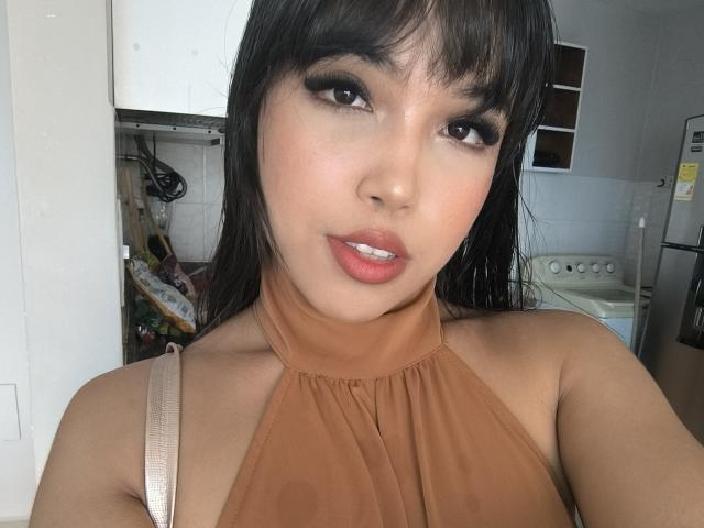 Heyly has a big ass and thick thighs, wearing an orange halter top, looking seductively at the camera with pink lips.
