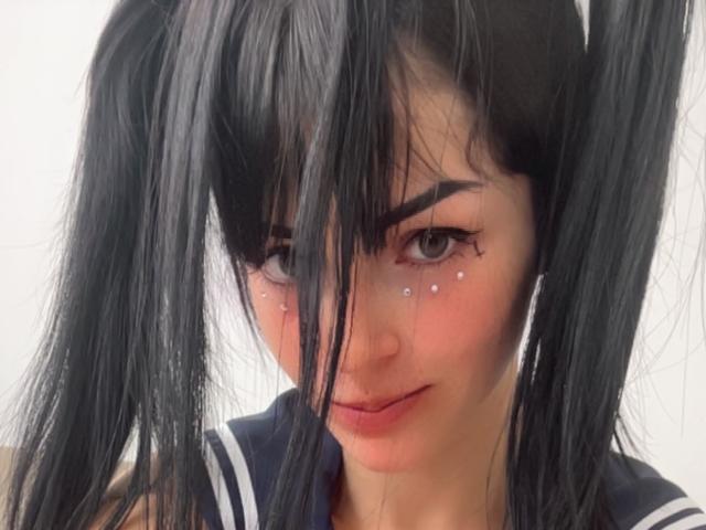 Liiil ha due codini neri, sopracciglia scure e minuscole macchie bianche sulle guance. Indossa una divisa scolastica blu scuro e bianca e ha un leggero sorriso..
