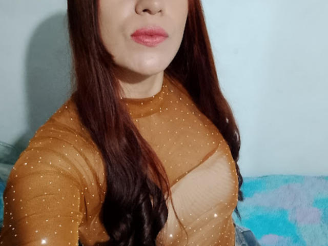 SofiaFountaine with brown hair, wearing a sheer, golden-brown top that reveals her small tits, pink lips, and light skin. Her nipples are slightly visible through the fabric.