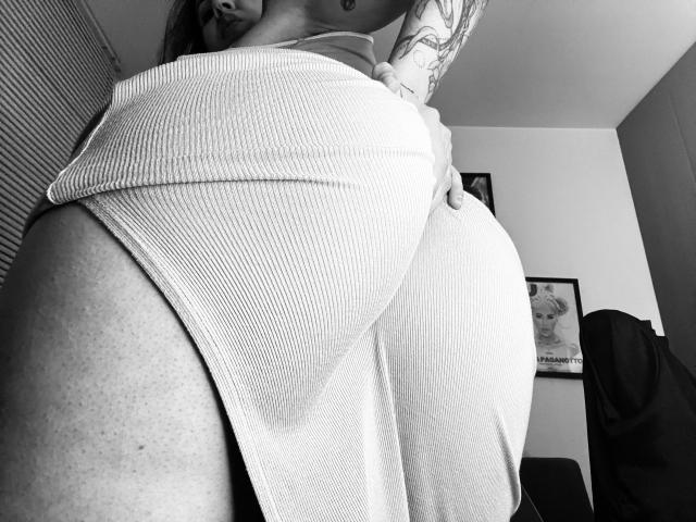 SujannaVarma's ass in a tight, ribbed, white dress, showing her big, round, and curvy butt. Her tattooed arm is partially visible. Black-and-white, low-angle shot.