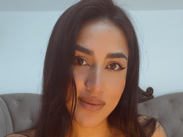 Alana Harris ha lunghi capelli neri, un piercing al naso e un trucco occhi con l'eyeliner allungato. Sta guardando la fotocamera con un leggero sorriso, mostrando le sue labbra piene..