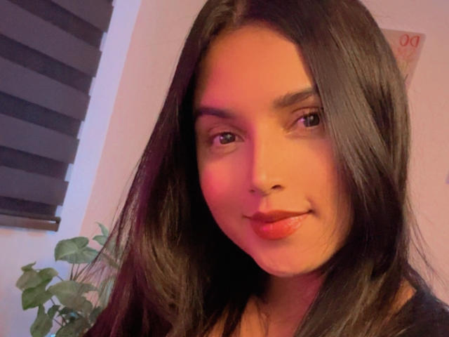 VeronicaFire69 has long, straight black hair and is smiling with red lipstick, looking slightly to the side. Her cute ass is not visible in this image.