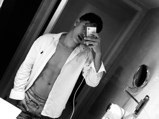 Black-and-white selfie of LyannG, shirt open to reveal a toned, bare chest with visible abs, wearing jeans with "PUMA" waistband, holding phone, mirror reflection.