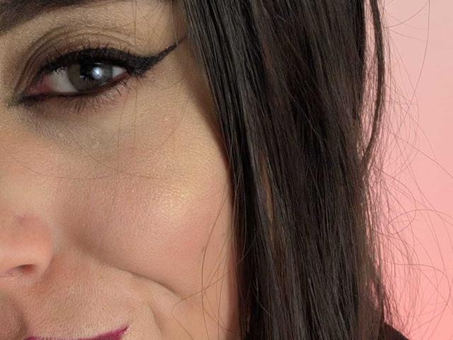 KimyR's face with brown eyes, black eyeliner, and straight dark hair, showing her left cheek and partial smile, pinkish skin tone, and subtle makeup.
