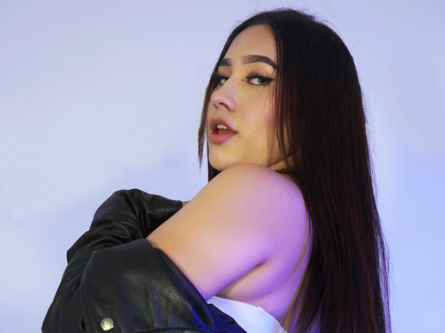 CelesteRusso with long dark brown hair, looking over shoulder, black leather jacket falling off white top, exposing shoulder, sultry expression, slight blue and purple lighting.