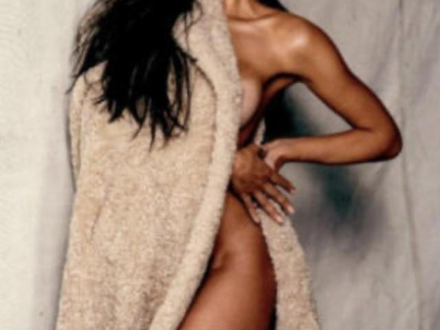 LaVenusFrench with long black hair, nude, wearing a beige fuzzy coat, hand on hip, covering tits and ass, coat open, showing her brown, toned, sexy body.