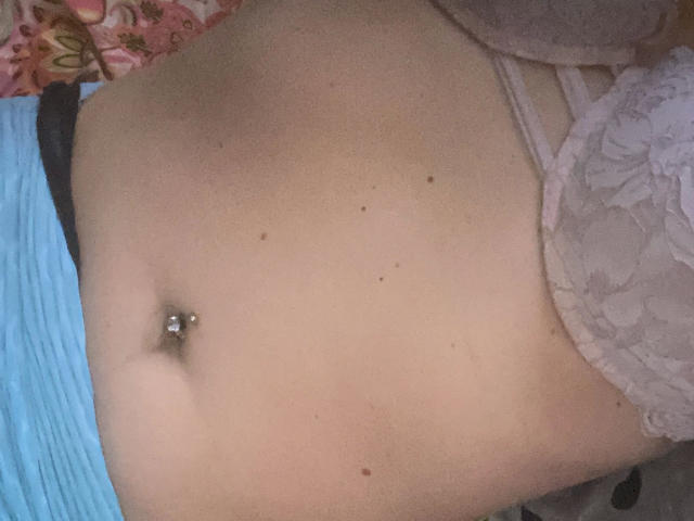 Melli-hot's flat stomach with a navel piercing, wearing light purple lace panties, and a blue garment partially visible on the left side of the image.