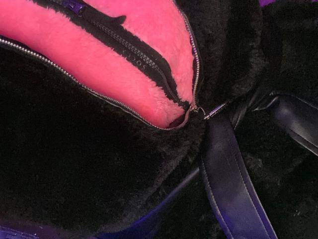 Melli-hot's black zip-up jacket is partially unzipped, revealing pink, fluffy inner lining with a black zipper. Black leather straps are visible on the right.