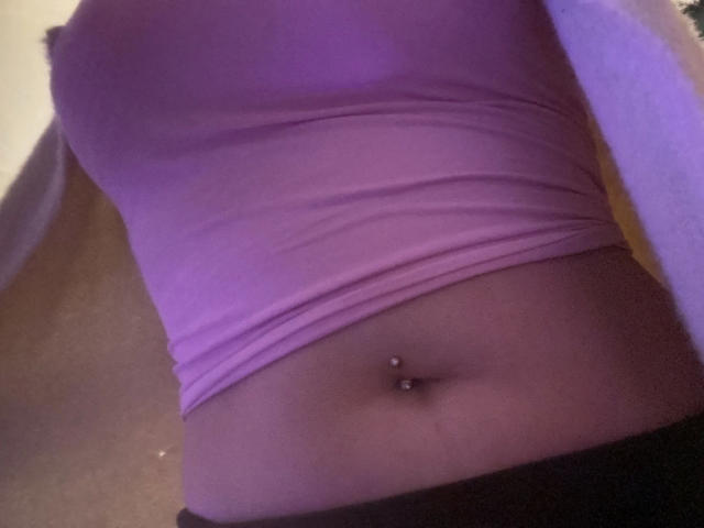 Melli-hot's purple tank top, showing a pierced belly button, with her black pants down, revealing her flat, tan stomach. The image focuses on her midsection.