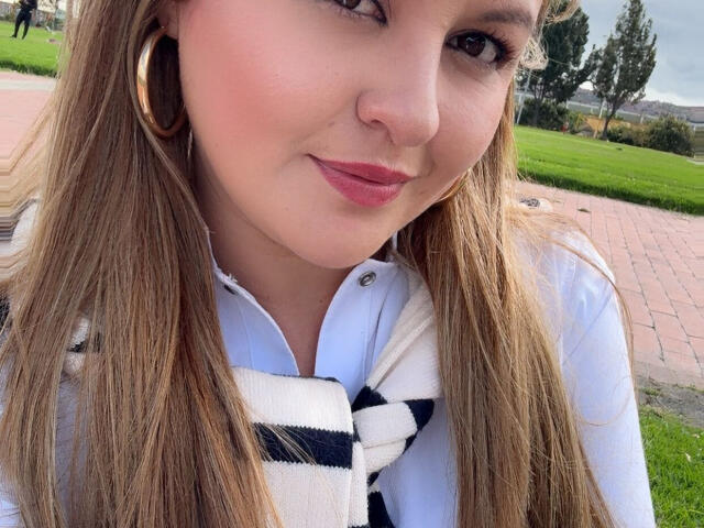 LaurenSpitz with long blonde hair, pink lipstick, white shirt, black-and-white scarf, and gold hoop earrings, smiling slightly, showing her cute nose and cute tits.