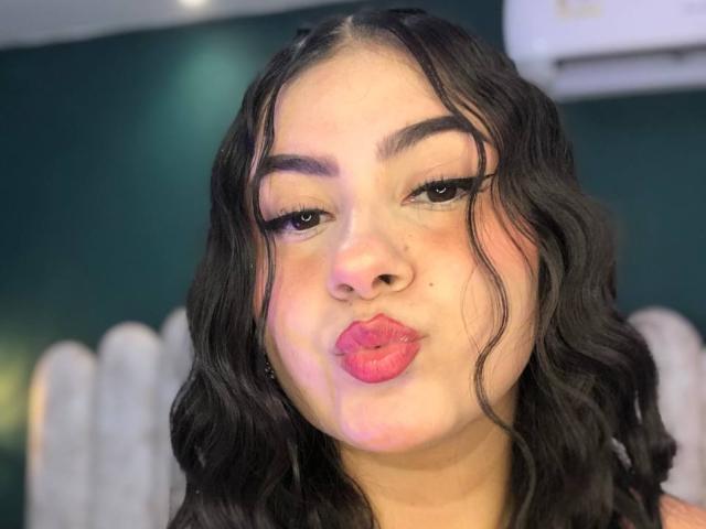 AlanaaWalker with wavy black hair, thick eyebrows, pink lipstick, and long eyelashes pouting her full, glossy lips. Her light brown skin is slightly flushed.