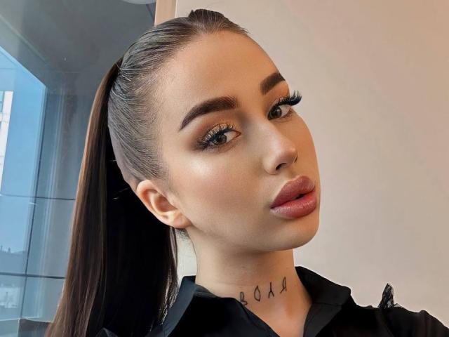 IsabelleDelicious heeft een paardenstaart, dikke wenkbrauwen, lange wimpers, roze lippenstift en een tatoeage op haar nek met zwarte lijnen. Ze draagt een zwart shirt..