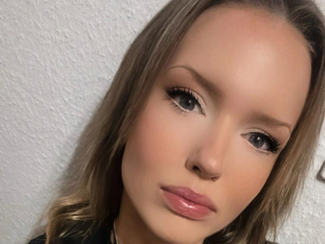 Sweet-Ida-hot's face, featuring light brown hair, glossy pink lips, and long eyelashes, with a slight, neutral expression and smooth, fair skin.