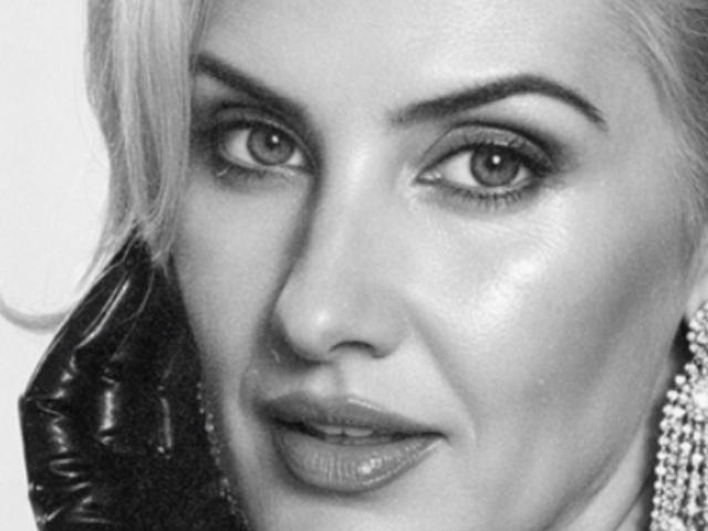 TianaQLove's face in a black-and-white photo, showing her shiny skin, full lips with gloss, and her piercing eyes, with a leather ear piece on the left side.