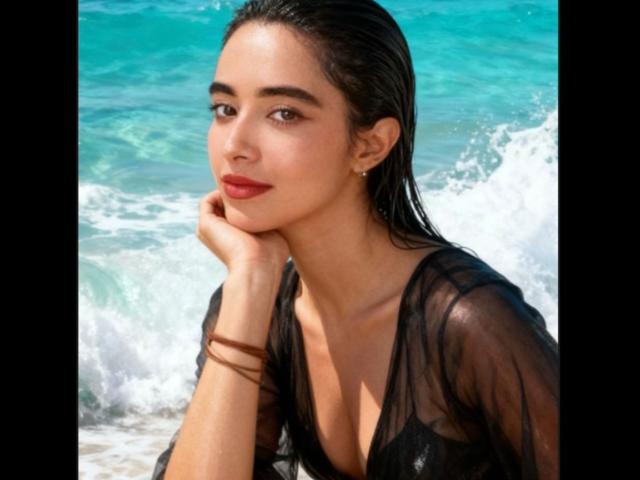 VivienneLaurent with wet black hair, red lipstick, and a sheer black top, leaning on her hand by the turquoise ocean. She's got a cute ass and a sexy look.