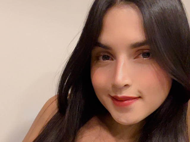 VeronicaFire69 has long black hair, a cute smile, and red lipstick, with a slight blush on her fair skin, and she's looking directly at the camera.