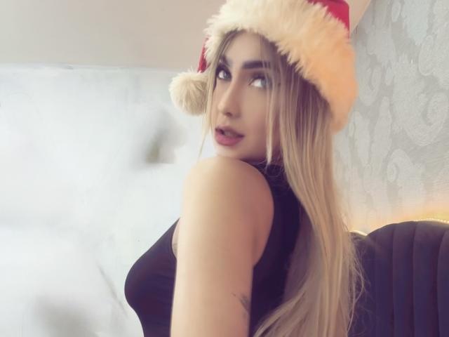 VictoriiaGrey with long blonde hair, wearing a red Santa hat and black sleeveless top, looking over her shoulder, showing her ass, with a tattoo on her upper arm.