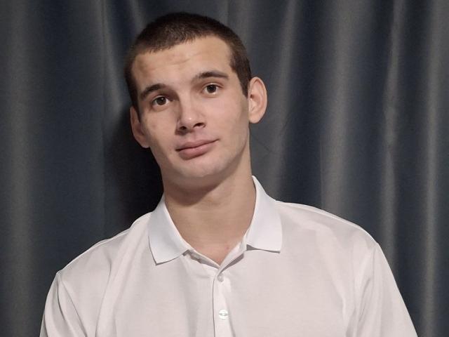 Noctyve with short brown hair, white shirt, and slightly tilted head, looking to the side with a subtle smile. Noctyve's face is clean-shaven with a slight nose bump.