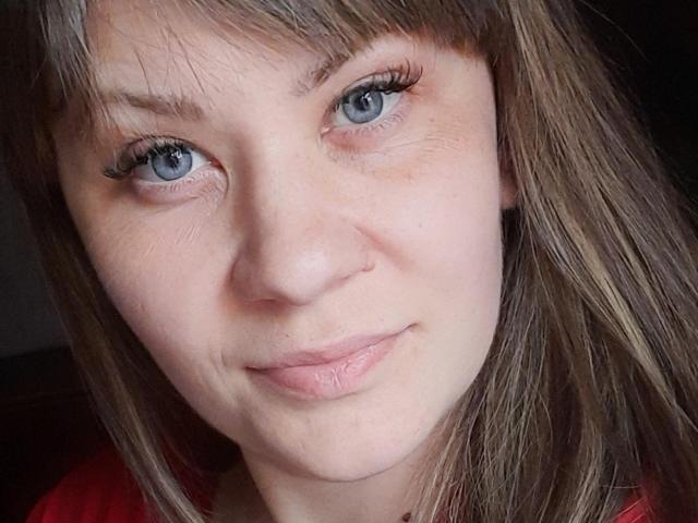 EmilyLunar has blue eyes, light brown straight hair with bangs, a small nose, and a subtle smile with slightly parted lips. Her skin is pale with visible freckles.