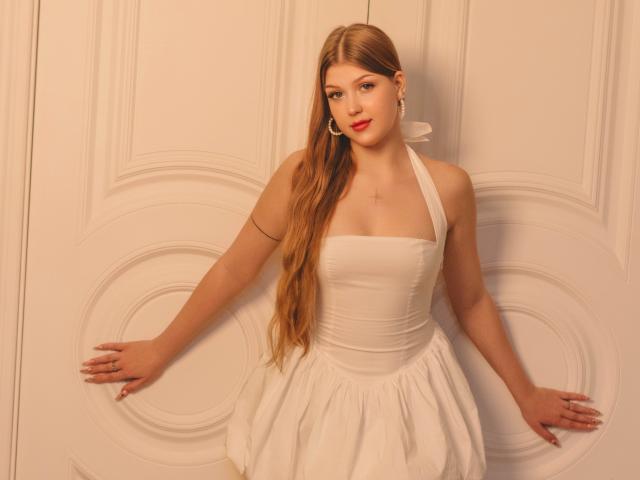 StellaLane with long blonde hair, white halter dress, and red lipstick, standing with arms out, hands on wall, wearing hoop earrings, showing her tits and ass.