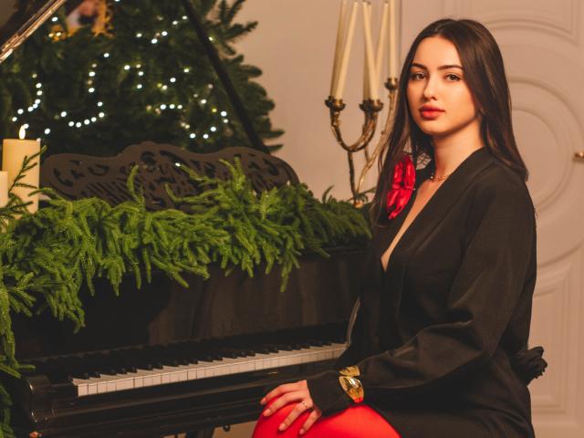 ChristinaBliss with medium tits, black dress, red gloves, and necklace, sitting at a piano with green foliage, candles, and a Christmas tree in the background.