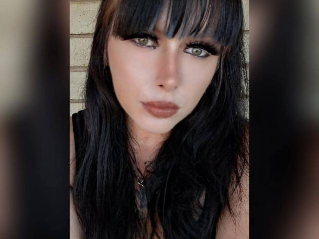 Kasarity has dark black hair with bangs, green eyes, and full lips. She's wearing black eyeliner and a black top. Her face is centered in the shot.