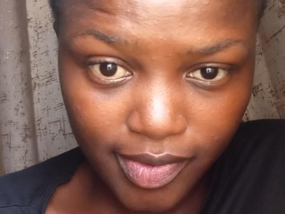 Lollasavage's face, brown skin, dark eyebrows, small nose, tongue slightly out, black shirt, shiny eyes, short hair, subtle smile, slightly textured skin, close-up, serious expression.