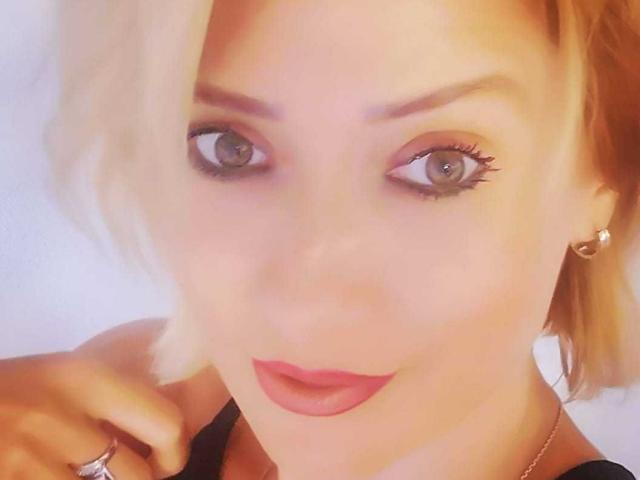 AnimatedBloat has pale skin, blue eyes, and pink lipstick. Blonde hair is partially covering her right eye. She's wearing a black top and a small hoop earring.