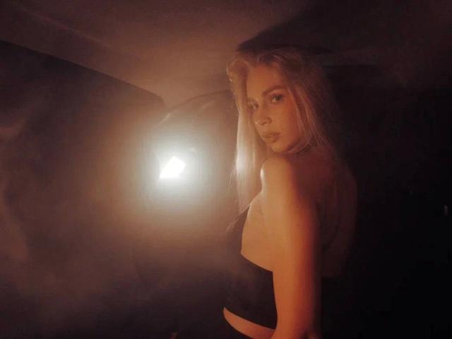 BlondiAngel-hot with long blonde hair, looking back over shoulder, wearing black strapless top, glowing light in dark background, subtle makeup, sexy, soft light, warm tones.