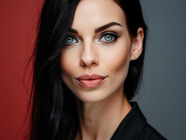 CassieBest has blue eyes, black hair, and pink lips. She's looking at the camera with a slight smile. She's wearing a black shirt. Her tits are small.