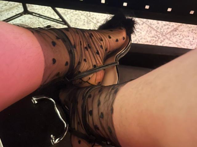 Close-up of SteffanyTaylor's feet in sheer black polka dot stockings, showing the textured fabric and black strappy high heels with furry accents. The feet are slightly parted, revealing a hint of pinkish skin between the toes. The stockings have small, evenly spaced black dots. The angle is from above, highlighting the detailed texture and pattern of the stockings.