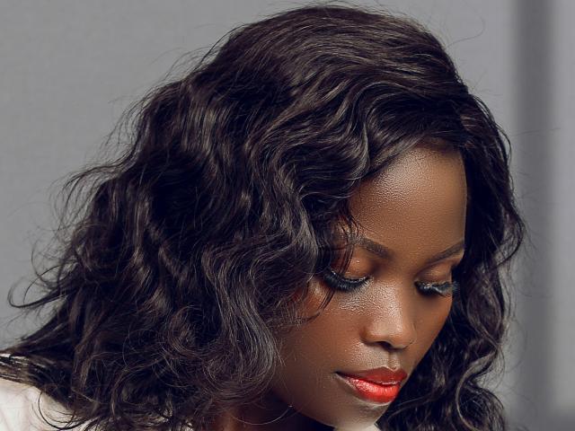 CamiliaWanda has dark, wavy hair, red lipstick, and blue eyeshadow. Her eyes are closed, and she has a smooth, brown skin tone. She's looking down with a gentle expression.