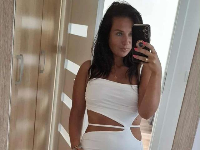 CuteLexy-hot with dark hair, wearing a white, cut-out dress, holding a phone in a mirror selfie, showing small tits, and a cute face with pink nails.