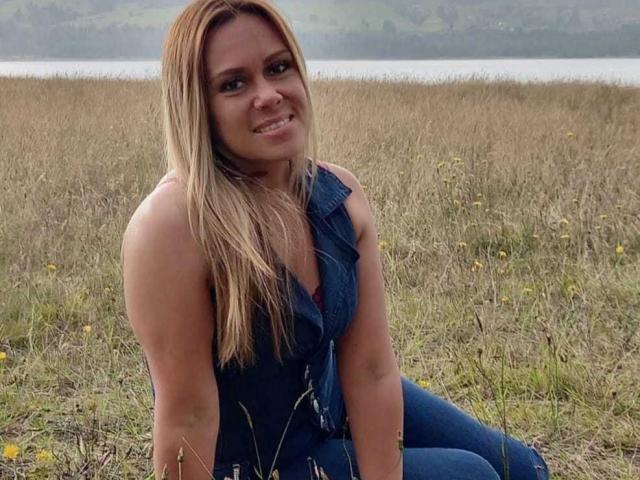 LilithBonneth with long blonde hair, smiling, wearing a sleeveless denim vest and jeans, sitting in a grassy field with yellow flowers, showcasing her tits and ass.