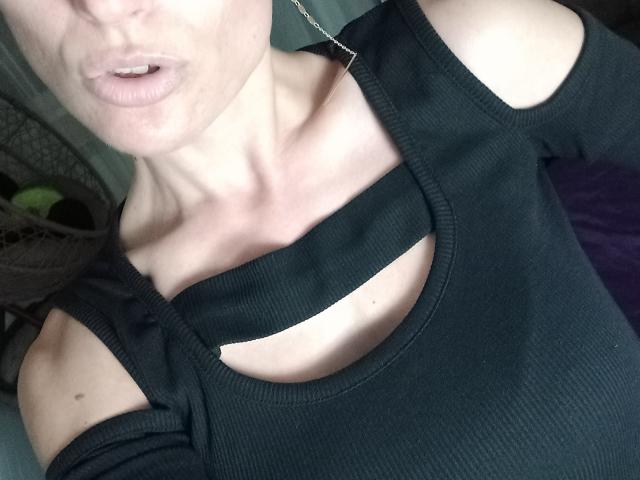 BellaJulls with pale skin, parted lips, wearing a black ribbed top with cut-out shoulders, exposing a small portion of her tits. Necklace visible, upper body in focus.