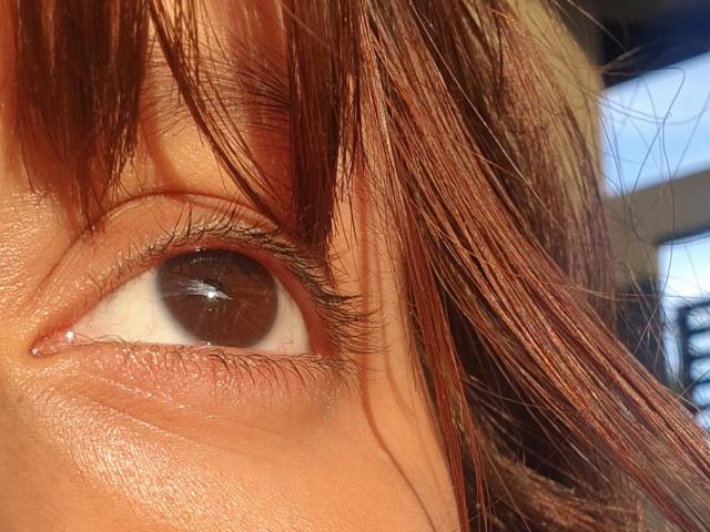 ArenaPeeach's bruine oog met zichtbare wimpers, licht gerimpelde huid en bruinrode haarlokken in het beeld, in fel zonlicht..