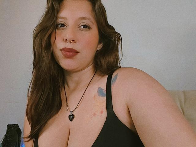 ArenaPeeach a les cheveux bruns et ondulés, un anneau de nez et porte un débardeur noir qui met en valeur ses grandes seins. Elle sourit et a un tatouage sur son épaule droite..