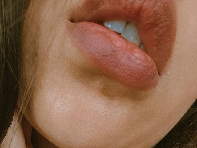 ArenaPeeach's plump, red-tinged lips are slightly parted, showing a hint of white teeth. Her skin is smooth, with a subtle tan. The focus is on her glossy lips.