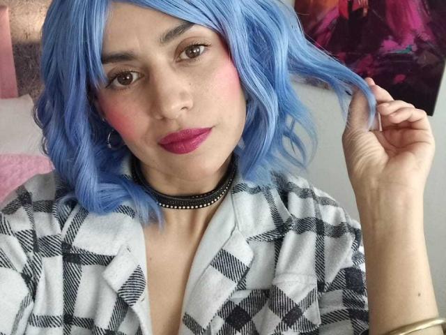 LilaaSalmon with blue hair, pink blush, red lipstick, checkered shirt, black choker, holding hair, light skin, subtle makeup, pink nail, purple eye shadow, slight smile, looking at camera.